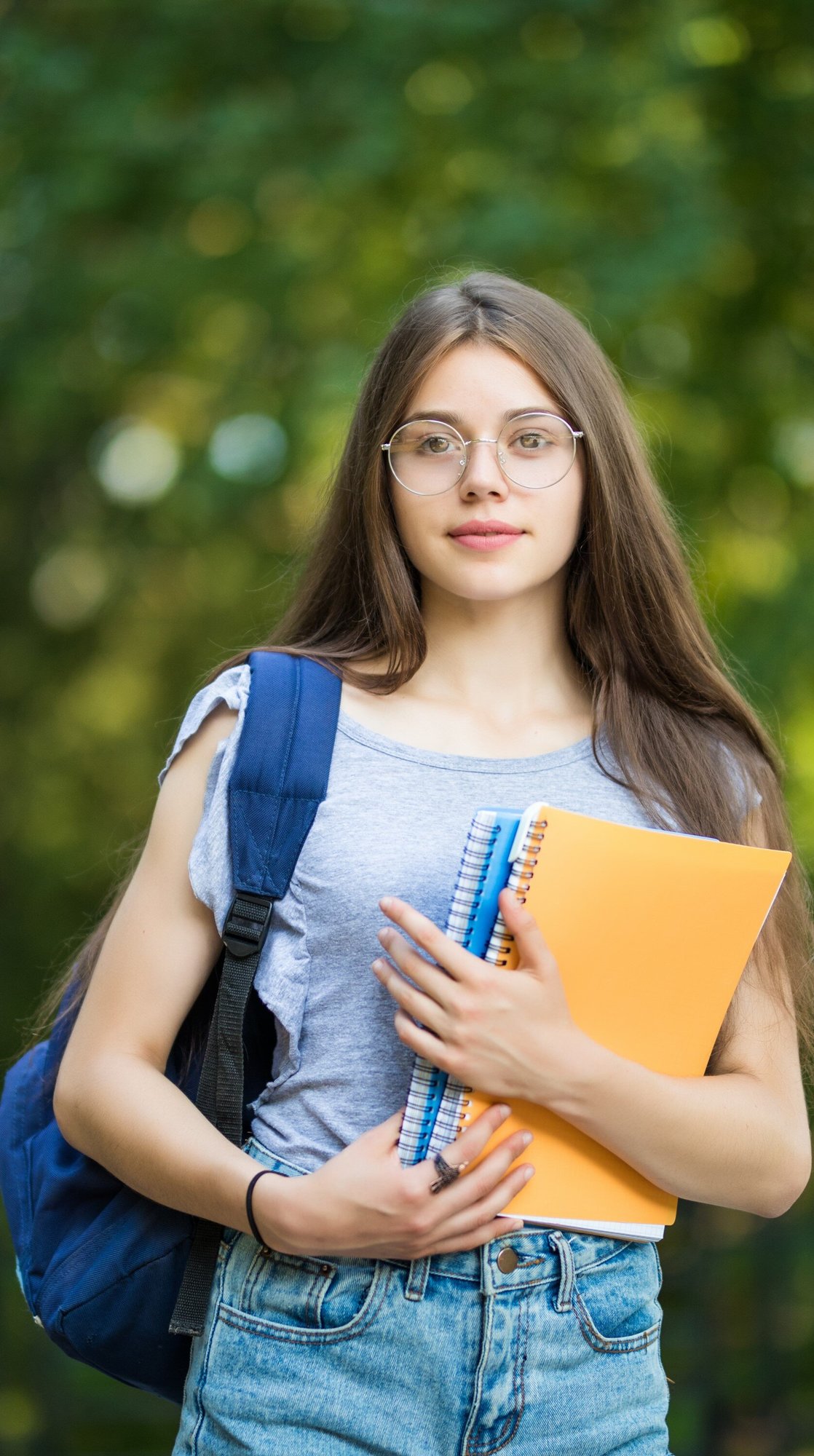 cheerful-attractive-young-woman-with-backpack-notebooks-standing-smiling-park