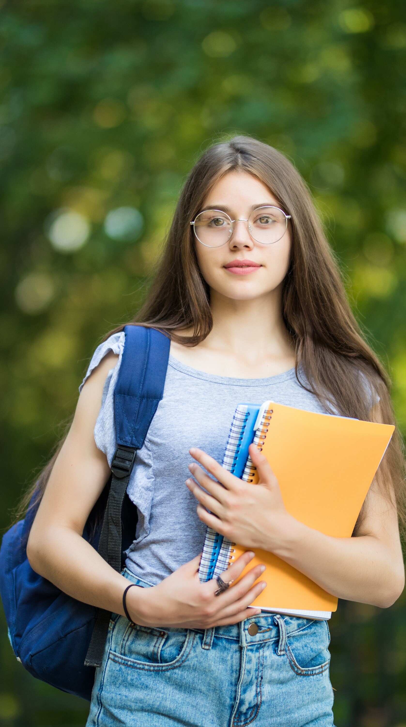 cheerful-attractive-young-woman-with-backpack-notebooks-standing-smiling-park